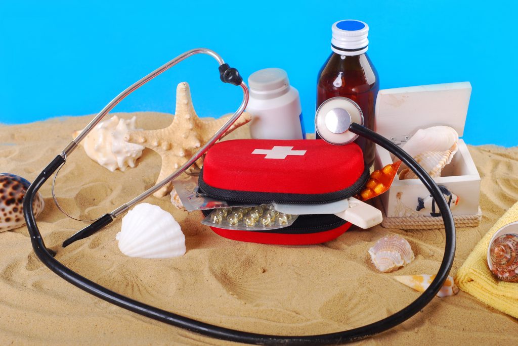 first aid box with medicines,thermometer and stethoscope on the beach as healthy travel tips