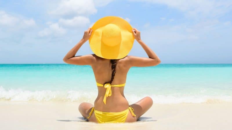 woman in a yellow bikin sitting on the beach holding a yellow hat