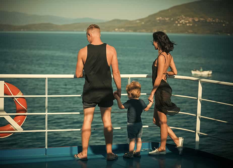 Family travelling on cruise ship on sunny day. Father, mother and child stand on deck.