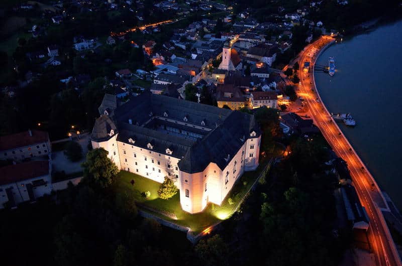 Aerial night view of Greinburg Castle in Grein, Austria, illuminated against the Danube River, showcasing its historic architecture and charming riverside town.