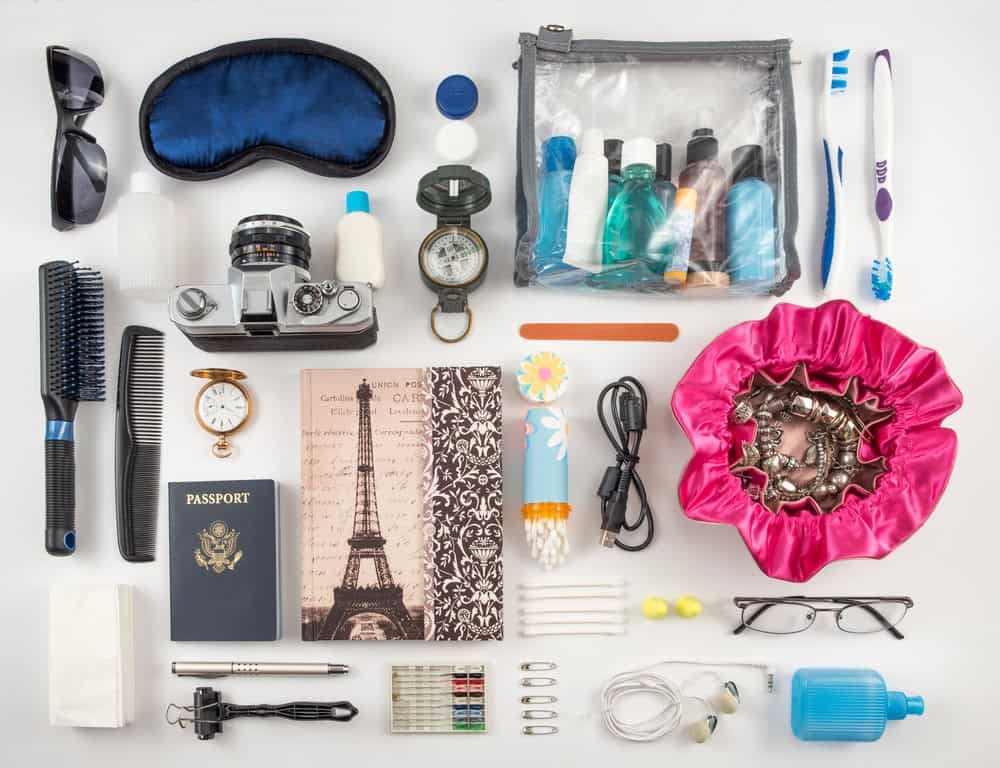 A neatly arranged flat lay of travel essentials, including toiletries, a passport, sunglasses, a camera, and a sleep mask, demonstrating how to pack light for travel.