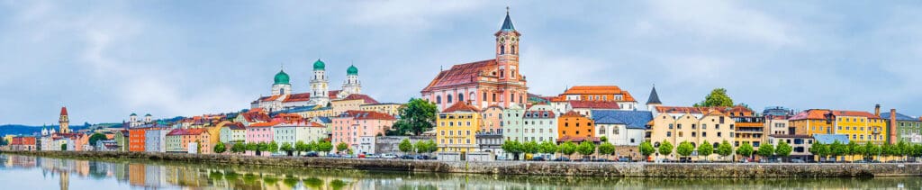 Scenic view of Passau, Germany, along the Danube River featuring colorful historic buildings and St. Stephen's Cathedral. A must-visit stop on a luxury Danube cruise on AMAWaterways.